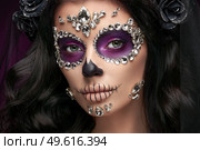 Portrait of a woman with sugar skull makeup over purple background. Halloween costume and make-up. Portrait of Calavera Catrina. Стоковое фото, агентство Ingram Publishing / Фотобанк Лори