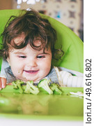 Baby eating food in her green highchair. Стоковое фото, агентство Ingram Publishing / Фотобанк Лори