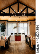 The presidium of the newlyweds in the banquet hall of the restaurant is decorated with candles and green plants, wisteria hangs from the ceiling. Стоковое фото, агентство Ingram Publishing / Фотобанк Лори