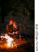 Young couple a guy and a girl in bright knitted hats stopped at a camping near the fire. Стоковое фото, агентство Ingram Publishing / Фотобанк Лори