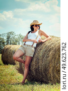girl with black hair in beige wool coats and suspenders stands near the haystacks. Стоковое фото, агентство Ingram Publishing / Фотобанк Лори