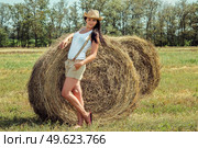 girl with black hair in beige wool coats and suspenders stands near the haystacks. Стоковое фото, агентство Ingram Publishing / Фотобанк Лори