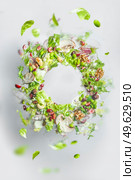 Circle frame of flying healthy green salad with lettuce, nuts, beans, dressing and vegetables. Balanced vegan food with copy space. Levitation of food. Стоковое фото, агентство Ingram Publishing / Фотобанк Лори
