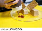 Unrecognisable chef squeezing drops of jam onto a plate of foie micuit with crunchy croutons while working in a restaurant. Crop chef plating foie micuit with crunchy croutons in restaurant. Стоковое фото, агентство Ingram Publishing / Фотобанк Лори