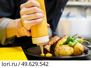 Unrecognizable cook pouring gaucho sauce on a plate of ribs with delicious roast potatoes served with peppers at the restaurant.. Anonymous chef plating roasted ribs with potatoes. Стоковое фото, агентство Ingram Publishing / Фотобанк Лори