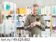 Senior man in pharmacy scans QR code on ointment for bruises. Стоковое фото, фотограф Яков Филимонов / Фотобанк Лори
