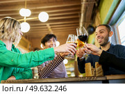 From below multiracial man and women smiling and clinking glasses of alcohol beverages over table while proposing toast during meeting in bar. Diverse friends clinking glasses over table in beautiful pub. Стоковое фото, агентство Ingram Publishing / Фотобанк Лори
