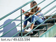 Young black woman with coloured braids, sitting on some steps while consulting her smartphone with her feet resting on a skateboard.. Black woman with coloured braids, consulting her smartphone with her feet resting on a skateboard. Стоковое фото, агентство Ingram Publishing / Фотобанк Лори