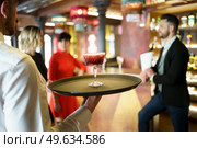 Back view of male bartender serving red cocktail on tray for company of elegant guests celebrating event in luxury restaurant. Waiter serving a cocktail for elegant clients in a nice bar. Стоковое фото, агентство Ingram Publishing / Фотобанк Лори