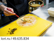 Anonymous cook spreading pine nut sauce on a plate of prawn carpaccio with capers while working in a restaurant kitchen.. Anonymous cook spreading pine nut sauce on a plate of prawn carpaccio. Стоковое фото, агентство Ingram Publishing / Фотобанк Лори