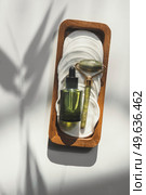 Beauty product setting with green bottle with pipette, jade massage roller and reusable cosmetic pads on white background with natural sunlight and shadow. Healthy skin care. Top view. Стоковое фото, агентство Ingram Publishing / Фотобанк Лори