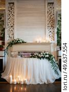 The presidium of the newlyweds in the banquet hall of the restaurant is decorated with candles and green plants, wisteria hangs from the ceiling. Стоковое фото, агентство Ingram Publishing / Фотобанк Лори