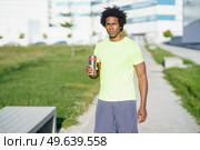 Tired African American male athlete standing with cup of water in street and having break during training in summer while looking at camera. Tired African American sportsman with water in city. Стоковое фото, агентство Ingram Publishing / Фотобанк Лори
