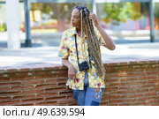 Beautiful African influencer combed with colorful braids standing with a camera outdoors.. African influencer combed with colorful braids standing with a camera outdoors. Стоковое фото, агентство Ingram Publishing / Фотобанк Лори