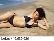 Relaxed African American female lying on the sand of a tropical beach sunbathing. Black girl tanning.. Relaxed African American female lying tanning on the sand of a tropical beach sunbathing. Стоковое фото, агентство Ingram Publishing / Фотобанк Лори