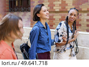 Group of positive multiracial female friends in colorful wear strolling together on street near brick building in city on summer day. Cheerful diverse women walking on street. Стоковое фото, агентство Ingram Publishing / Фотобанк Лори