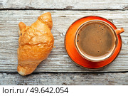 fresh boiled coffee served in beautiful orange cup with croissant around old style wooden background . close up. flat lay . Стоковое фото, агентство Ingram Publishing / Фотобанк Лори
