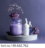 Purple beauty product setting with cosmetic serum bottles, candle and flowers. Healthy skin care products for facial treatment. Front view with copy space. Стоковое фото, агентство Ingram Publishing / Фотобанк Лори