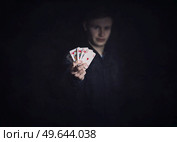 Successful poker player holds up a winning royal flush combination. Lucky gambler with playing cards on a dark background. Casino tournament winner, victory concept. Стоковое фото, агентство Ingram Publishing / Фотобанк Лори