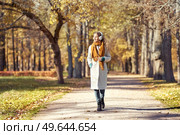 A young red-haired woman in a white coat walks in an autumn park. A girl listens to music in the autumn forest. Стоковое фото, агентство Ingram Publishing / Фотобанк Лори