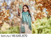 A young beautiful woman walks through the autumn park. A girl with a smartphone takes photos in an autumn forest. Стоковое фото, агентство Ingram Publishing / Фотобанк Лори