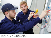 young electrician inspecting panel with voltmeter. Стоковое фото, агентство Ingram Publishing / Фотобанк Лори