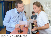 Man showing paperwork to lady at reception. Стоковое фото, агентство Ingram Publishing / Фотобанк Лори