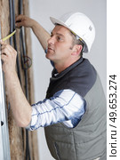workman measuring wall packed with insulation. Стоковое фото, агентство Ingram Publishing / Фотобанк Лори