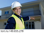 suited man wearing hardhat pointing towards residential property. Стоковое фото, агентство Ingram Publishing / Фотобанк Лори