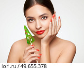 Beauty model girl eating Christmas tree shape lollipop.  Beautiful young woman with clean fresh skin. Girl beauty face care. Facial treatment. Cosmetology, beauty and spa. Red nails manicure. Стоковое фото, агентство Ingram Publishing / Фотобанк Лори