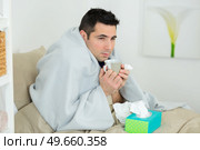 man wrapped in blanket holding hot drink and tissues. Стоковое фото, агентство Ingram Publishing / Фотобанк Лори