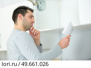 man fitting overhead kitchen cupboard reading instructions. Стоковое фото, агентство Ingram Publishing / Фотобанк Лори