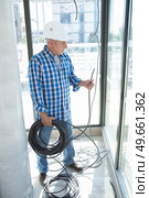 senior electrician holding reel of cable at indoor work site. Стоковое фото, агентство Ingram Publishing / Фотобанк Лори