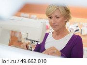 smiling middle aged woman using a sewing machine in laundry. Стоковое фото, агентство Ingram Publishing / Фотобанк Лори