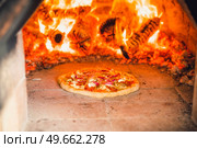 Pizza with toppings in a hot stone oven with fire wood baking a delicious meal. Стоковое фото, агентство Ingram Publishing / Фотобанк Лори
