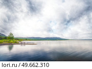 Lake scenery with a bench and a pine tree near the calm water and mountains in the background. Стоковое фото, агентство Ingram Publishing / Фотобанк Лори
