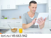 man reading news in tablet during breakfast in kitchen. Стоковое фото, агентство Ingram Publishing / Фотобанк Лори