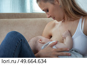 Nurturing Love a Mother Breastfeeds Her Baby Boy on a Beige Sofa. Стоковое фото, фотограф Aleksandr Golubev / Фотобанк Лори