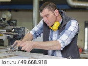 man wearing ear protectors cutting piece of wood. Стоковое фото, агентство Ingram Publishing / Фотобанк Лори