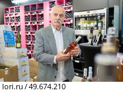 man in a supermarket comparing two wine bottles. Стоковое фото, агентство Ingram Publishing / Фотобанк Лори