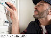 electrician with box of tools seating near distribution fuse board. Стоковое фото, агентство Ingram Publishing / Фотобанк Лори