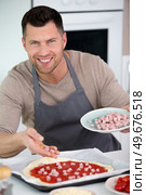 man adds ham topping to homemade pizzaman. Стоковое фото, агентство Ingram Publishing / Фотобанк Лори