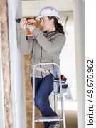 young woman on ladder with toolbelt using drill. Стоковое фото, агентство Ingram Publishing / Фотобанк Лори