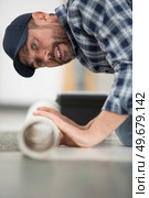 male worker unrolling carpet on floor at home. Стоковое фото, агентство Ingram Publishing / Фотобанк Лори