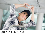 female electrician standing on scale to change light bulb. Стоковое фото, агентство Ingram Publishing / Фотобанк Лори