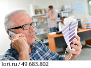 Man on telephone holding colour charts, looking skeptical. Стоковое фото, агентство Ingram Publishing / Фотобанк Лори
