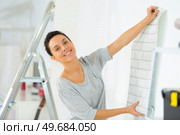 woman unrolling a wall paper on the wall. Стоковое фото, агентство Ingram Publishing / Фотобанк Лори