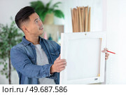 asian man deciding where to hang painting in the home. Стоковое фото, агентство Ingram Publishing / Фотобанк Лори
