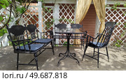 Metal furniture on terrace of old manor. Black chairs and table against background of white wooden lath wall of village house. Preparing for family tea party on sunny summer day. Gazebo in garden. Стоковое фото, фотограф Ирина / Фотобанк Лори