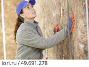 female worker packing insulation into framework on wall. Стоковое фото, агентство Ingram Publishing / Фотобанк Лори